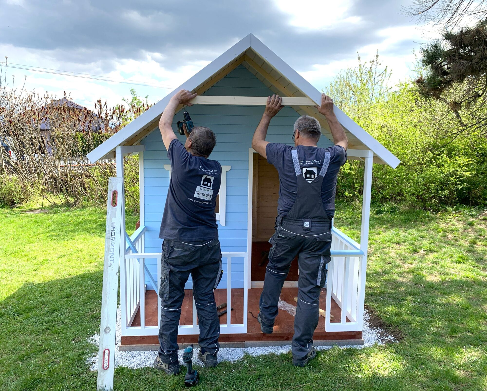 dvaja montážnici z&nbsp;firmy Záhradné domčeky pre deti montujú domček typ D v&nbsp;nebesky-modrej farbe